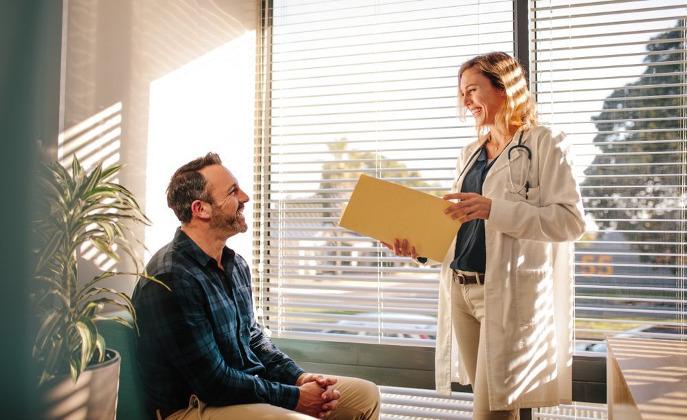 Doctor Discussing Alcohol Recovery Plan with Patient Smiling doctor holds file while talking to man about alcohol rehab