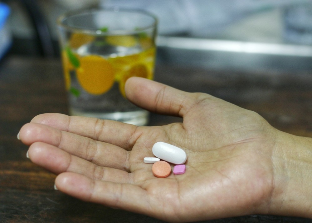 Effects of Alcohol on the Heart: Medication and Support Hand holding pills with a glass behind, effects of alcohol on the heart