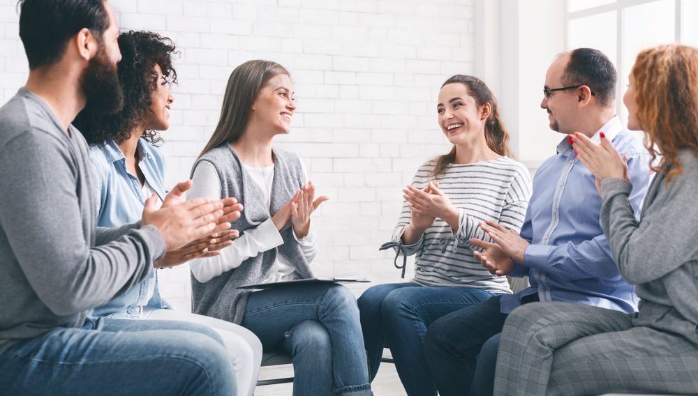 Supportive Group Therapy Session for Alcohol Recovery Diverse group of people in a rehab meeting clapping and smiling